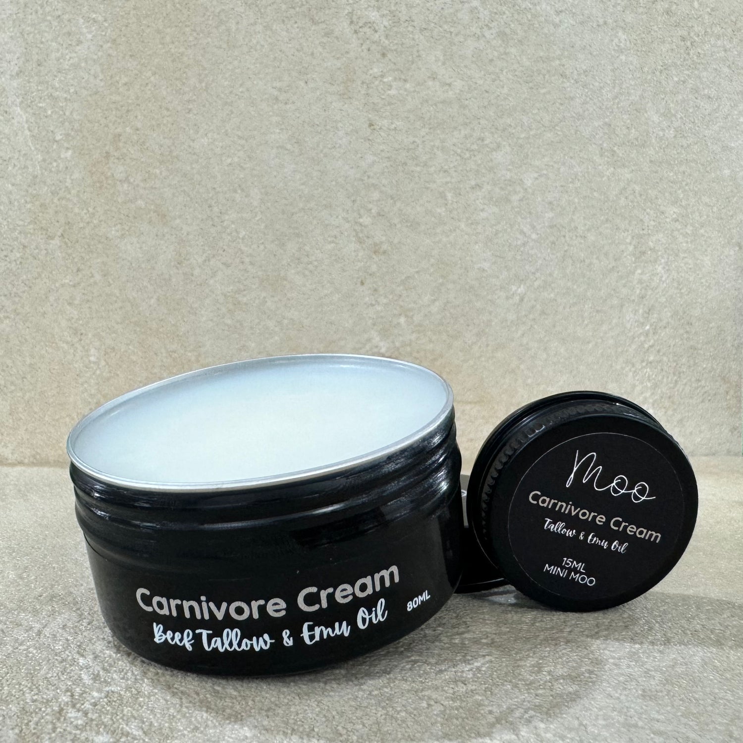 A black jar of Carnivore Cream with the lid off, showing the product inside. The label on the jar indicates that it is a beef tallow and emu oil cream.