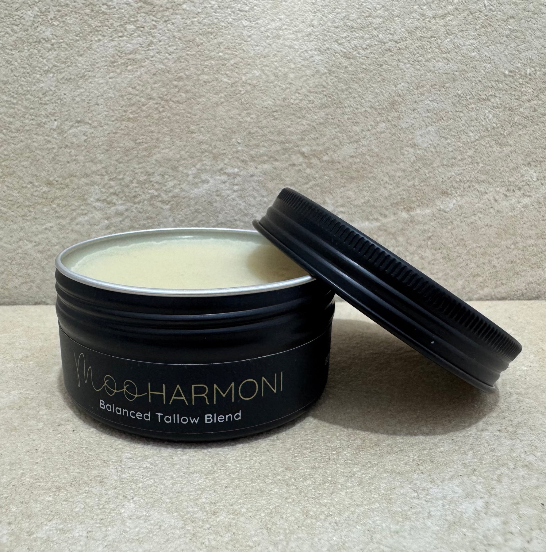 Black container of Moosharmoni Balanced Tallow Blend on a beige surface with a neutral background