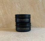 Two stacked black metal jars of Moo Harmoni Balanced Tallow Blend with gold lettering, set against a textured beige background.