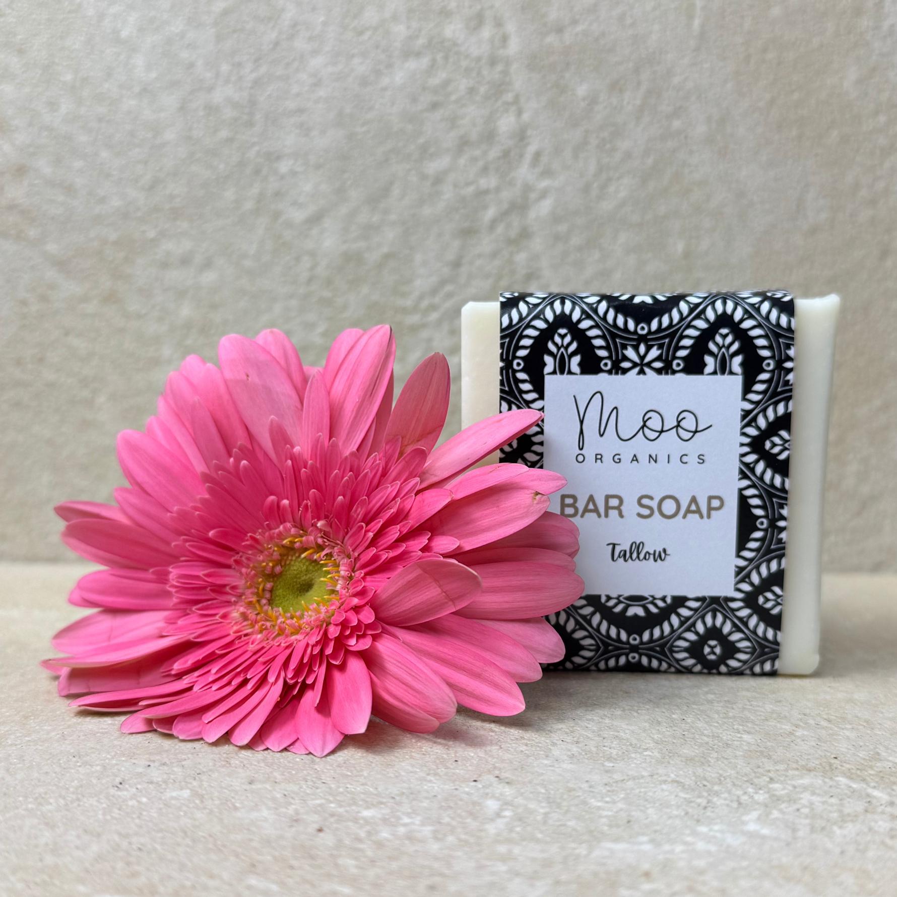 A packaged bar of Tallow Soap with the brand name Moo Organics displayed alongside a pink flower.