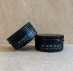 Two black metal tins of Sunny Dayz Tallow Based Zinc Cream on a textured beige surface against a matching beige background.