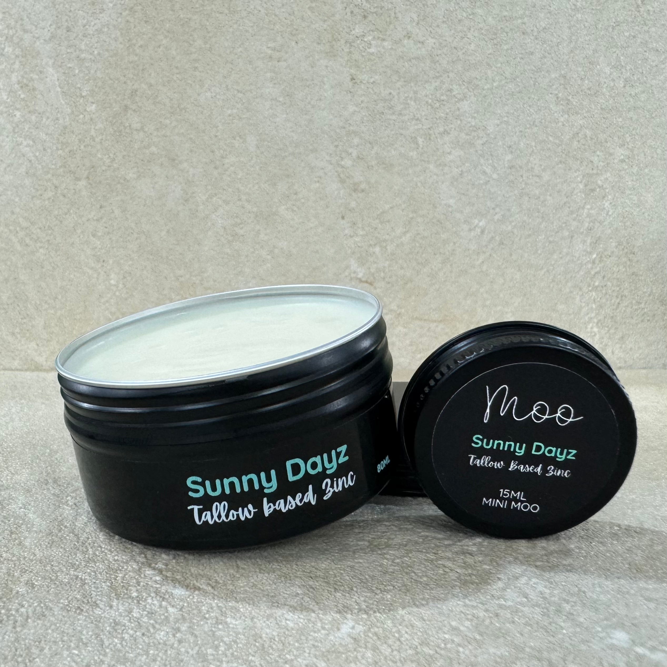 A jar of 'Sunny Dayz' tallow-based zinc, with its lid off, showing the white cream inside. The jar and lid have black labeling with green text.