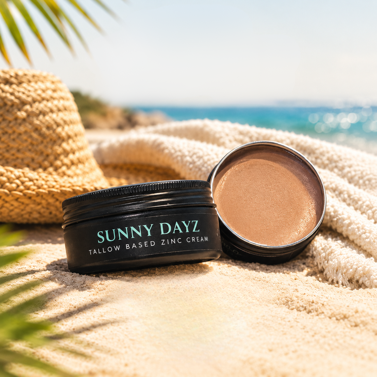 Black tin of sunny dayz on a towel with a hat at the beach