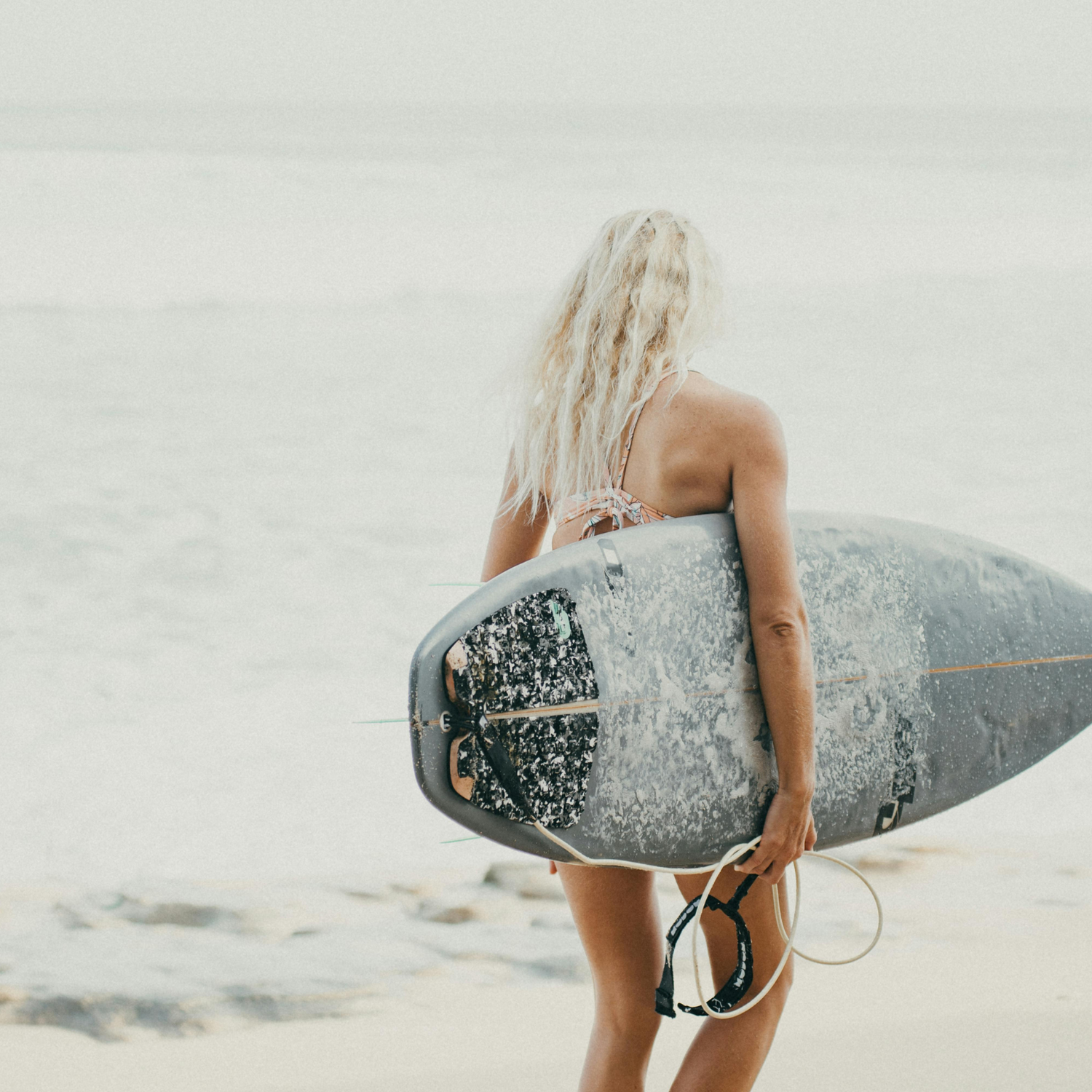 Surfboard Blonde Sun tallow by MOO, featuring a model with sun-kissed skin holding a surfboard, made with grass-fed beef tallow to naturally nourish, hydrate, and protect skin in a beach and surf environment