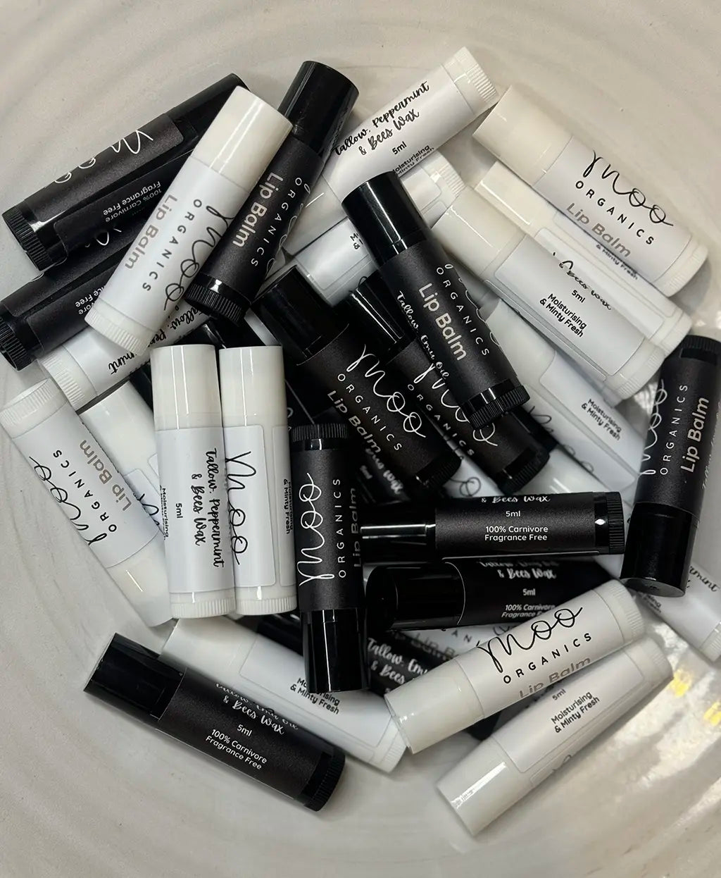 Sticks of Moo Organics lip balm, one labeled 'Tallow, Peppermint' and the other 'Organic', displayed on a textured surface.